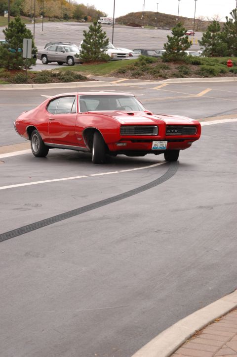 1985 Ford Crown Victoria LTD - A red 1969 Pontiac GTO is captured in a three-quarter front view, turning in a parking lot.