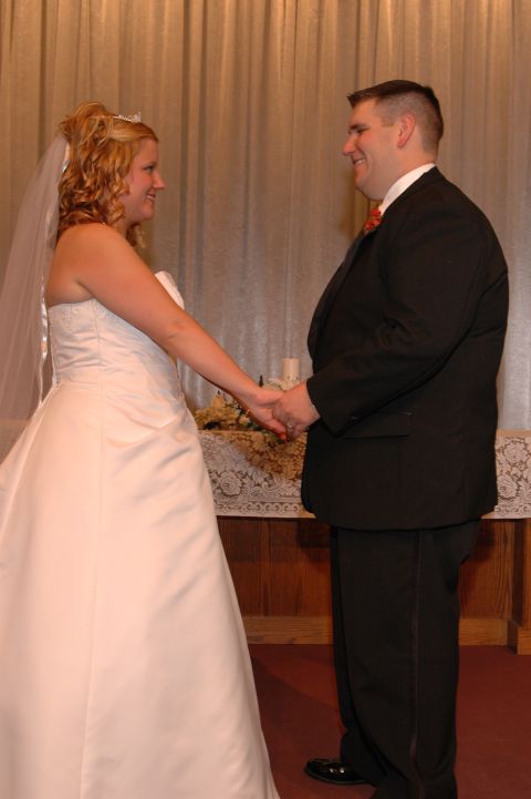 1985 Ford Crown Victoria LTD - A bride in a white gown and a groom in a suit hold hands during their wedding ceremony.