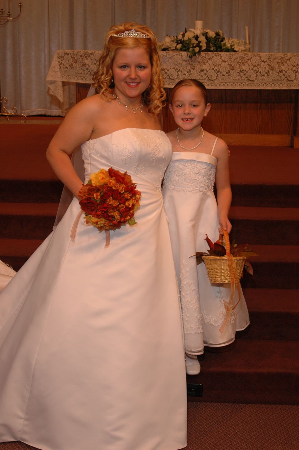 Bride and flower girl in wedding attire stand on steps in front of an altar