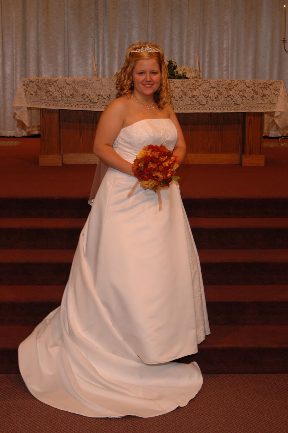 Bride in a white strapless wedding dress and tiara holding a bouquet of orange and red flowers