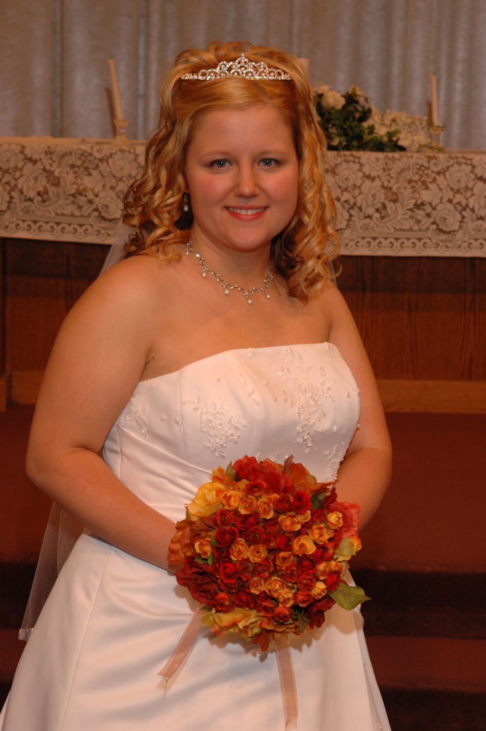 Bride in a white wedding dress and tiara holding an orange and red bouquet