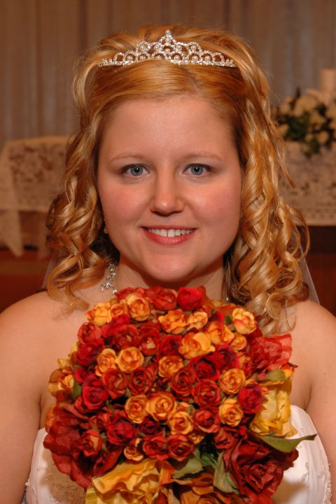 1985 Ford Crown Victoria LTD - A bride smiles while holding a bouquet of red and orange roses, wearing a tiara.
