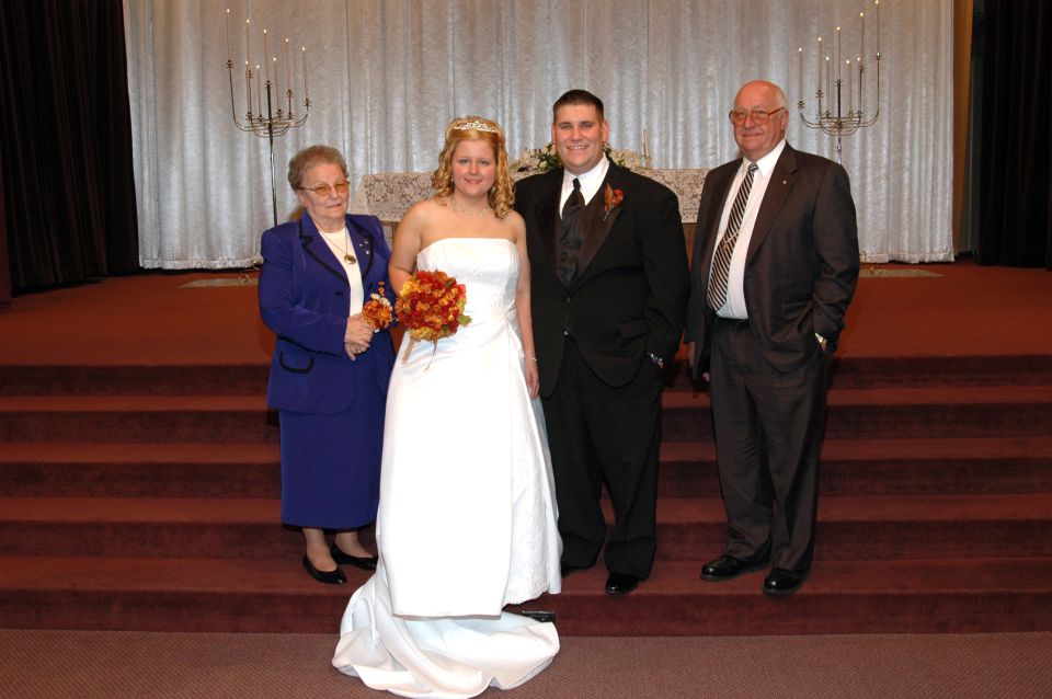 Bride, groom, and two older relatives pose for a photo in front of an altar
