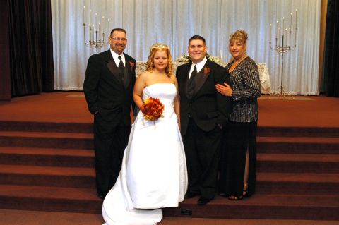 1985 Ford Crown Victoria LTD - A bride and groom pose with their parents on a set of red carpeted steps in front of an altar.