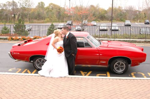 1985 Ford Crown Victoria LTD - A bride and groom share a kiss next to a bright red 1967 Pontiac GTO.