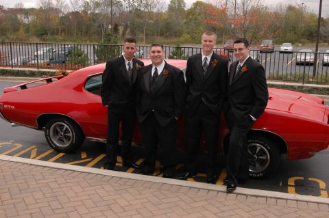 1985 Ford Crown Victoria LTD - A red 1969 Pontiac GTO is parked next to four men dressed in formal wear.