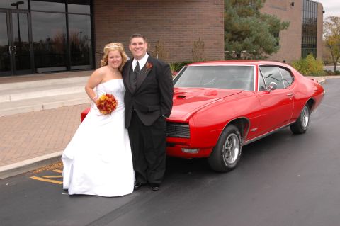 1985 Ford Crown Victoria LTD - A red 1967 coupe is parked next to a wedding couple outside a building.