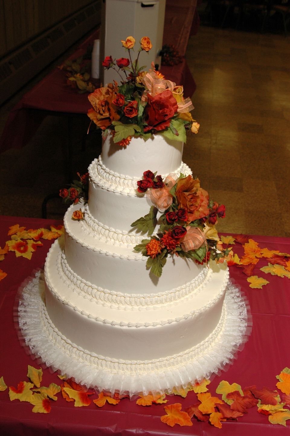 Four-tier white wedding cake decorated with autumn-colored flowers