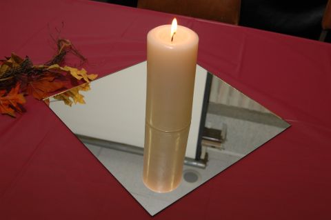 1985 Ford Crown Victoria LTD - A lit candle sits on a square mirror, surrounded by fall leaves on a red tablecloth, suggesting a decorative centerpiece.