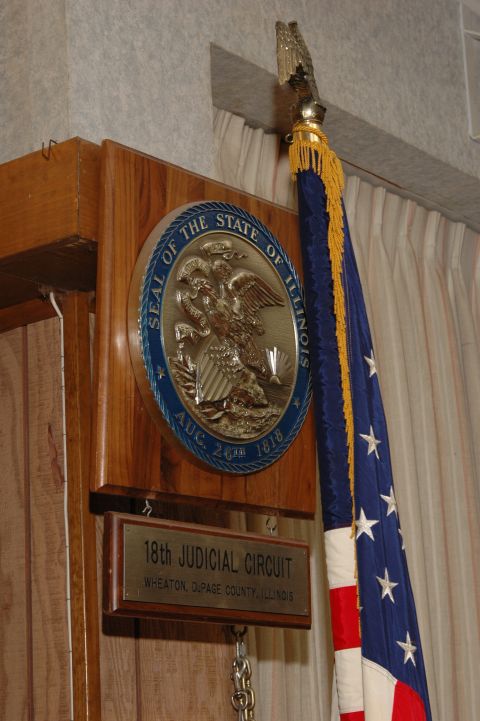 1985 Ford Crown Victoria LTD - A display the Seal of the State of Illinois and an American flag is shown next to a plaque for the 18th Judicial Circuit.