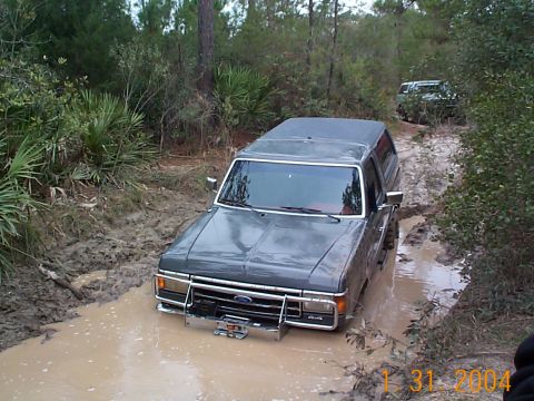 1992 Ford Bronco - A Ford Bronco navigates a muddy trail with another vehicle following behind.