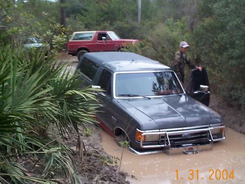 1992 Ford Bronco - A dark gray 1992 Ford Bronco is stuck in the mud, with a red Bronco visible behind it.