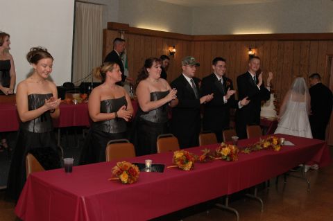1985 Ford Crown Victoria LTD - A wedding party applauds during a reception, with floral arrangements on the tables.