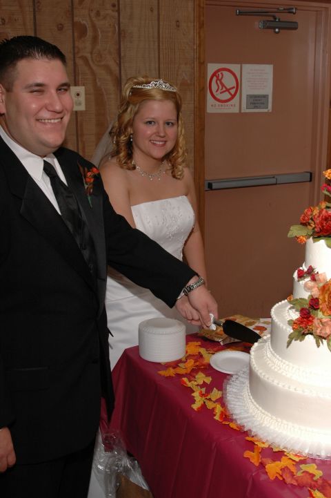 1985 Ford Crown Victoria LTD - A bride and groom smile as they cut into their wedding cake, decorated with fall-themed flowers.