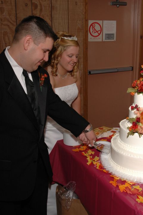 1985 Ford Crown Victoria LTD - A newlywed couple cuts into their wedding cake, adorned with autumn-colored flowers.
