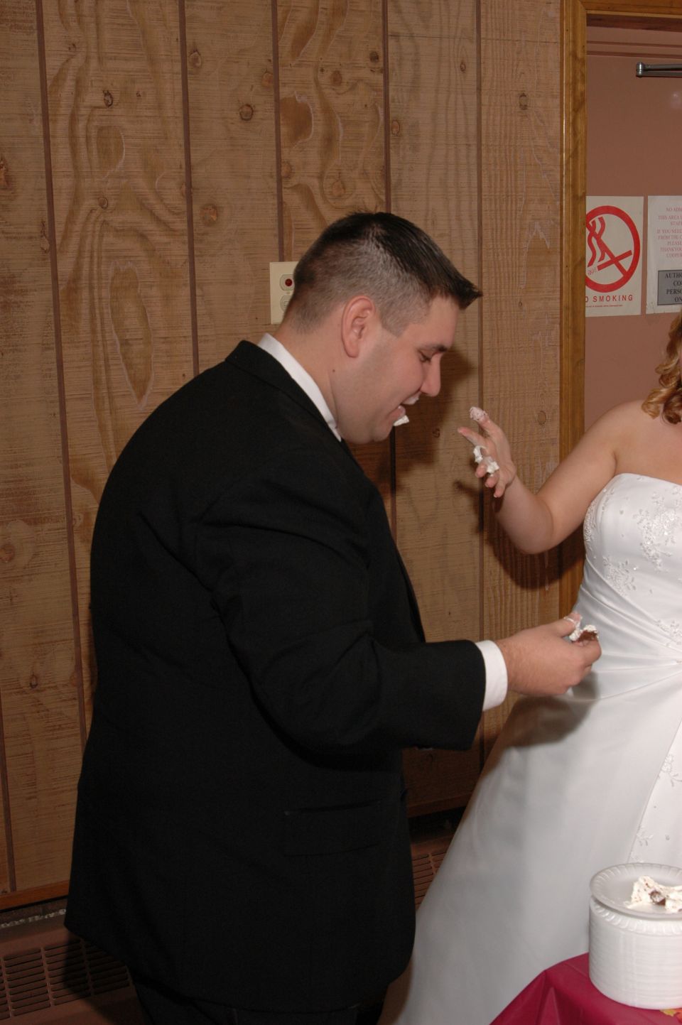 Groom with cake on face and hands, bride in wedding dress