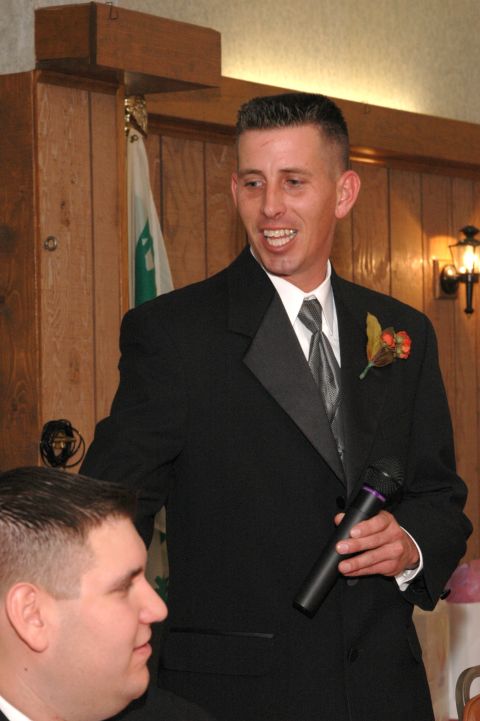 1985 Ford Crown Victoria LTD - A man in a tuxedo addresses an audience while holding a microphone at a wedding reception.