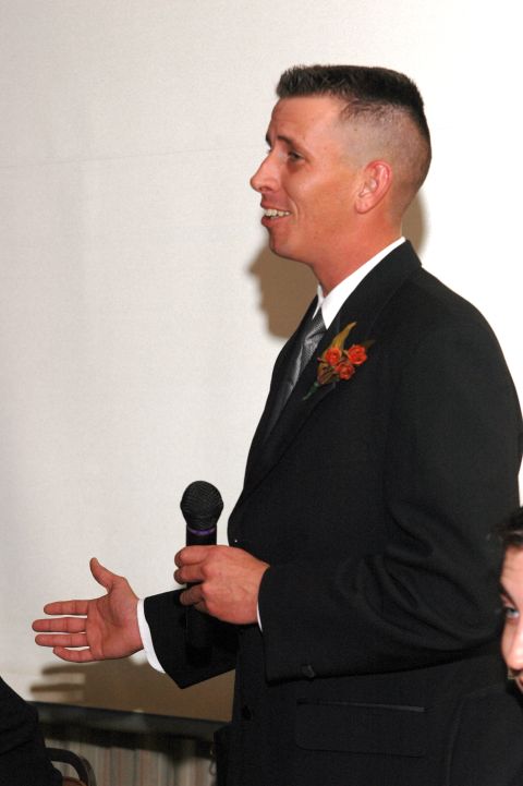 1985 Ford Crown Victoria LTD - Man in a suit speaks into a microphone at an event, possibly a wedding reception.