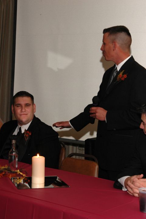 1985 Ford Crown Victoria LTD - A formal event with men in tuxedos seated at a table, one speaking into a microphone.