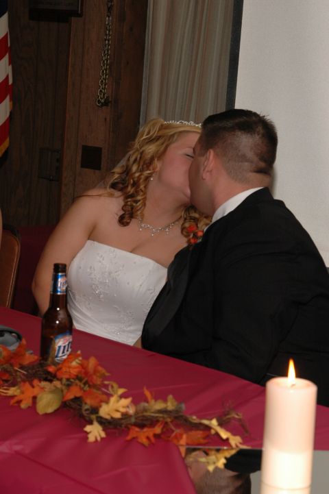 1985 Ford Crown Victoria LTD - A bride and groom share a kiss at their reception table, adorned with fall decorations and a lit candle.