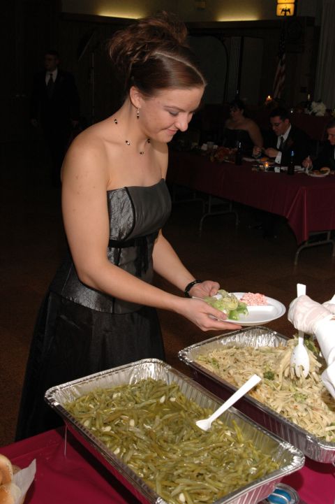 1985 Ford Crown Victoria LTD - A woman in formal attire serves food from large catering trays at a banquet or reception.