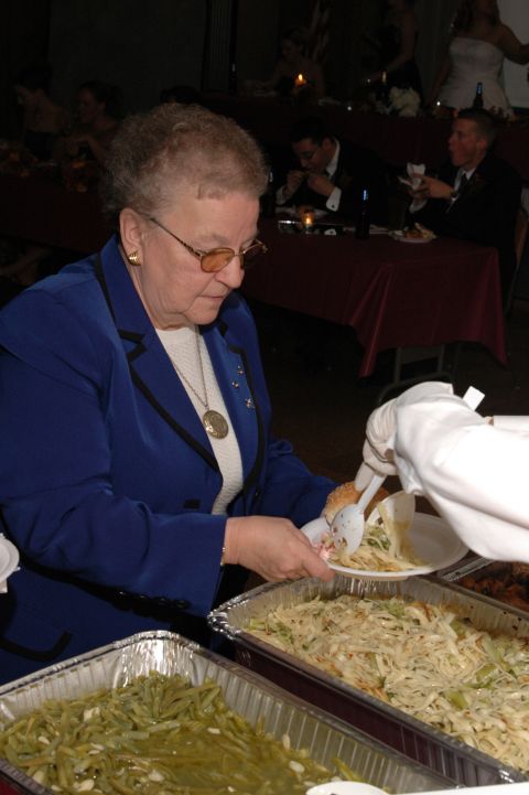 1985 Ford Crown Victoria LTD - A woman in a blue jacket is served food from a buffet at an event.