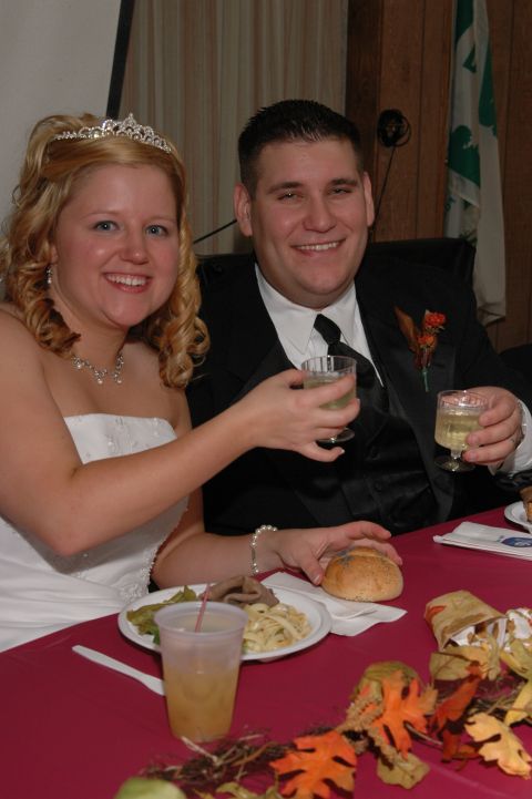 1985 Ford Crown Victoria LTD - A bride and groom raise their glasses in a toast during their wedding reception, surrounded by guests and festive decorations.