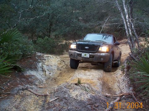 1992 Ford Bronco - A black Ford Ranger navigates a challenging off-road trail with steep inclines and loose dirt.
