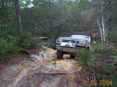 1992 Ford Bronco - Two vehicles navigate a challenging off-road trail through a wooded area.