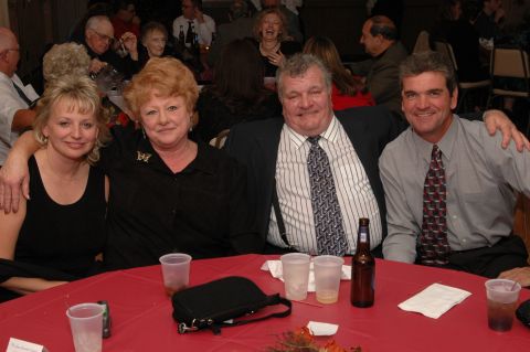 1985 Ford Crown Victoria LTD - A group of four people are seated at a red-clothed table, smiling and enjoying drinks at an event.