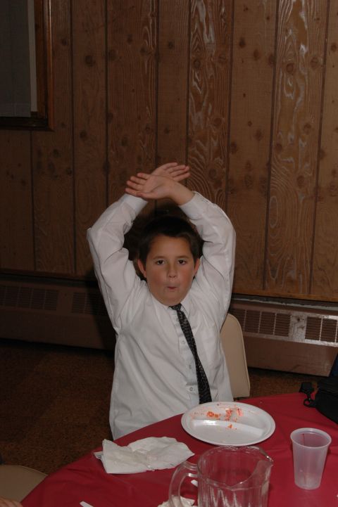1985 Ford Crown Victoria LTD - A young boy in formal attire sits at a table with a plate and cup, making a gesture with his arms.