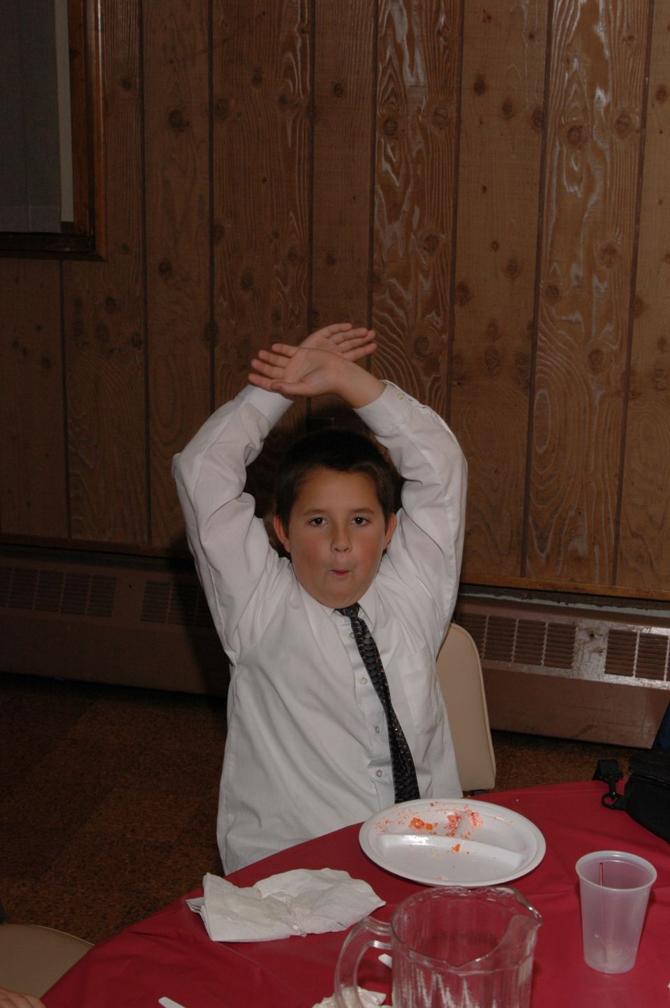 Kid in a white shirt and tie with arms crossed over head