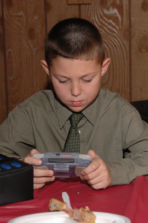 1985 Ford Crown Victoria LTD - A young boy dressed in a shirt and tie is engrossed in playing a handheld video game.
