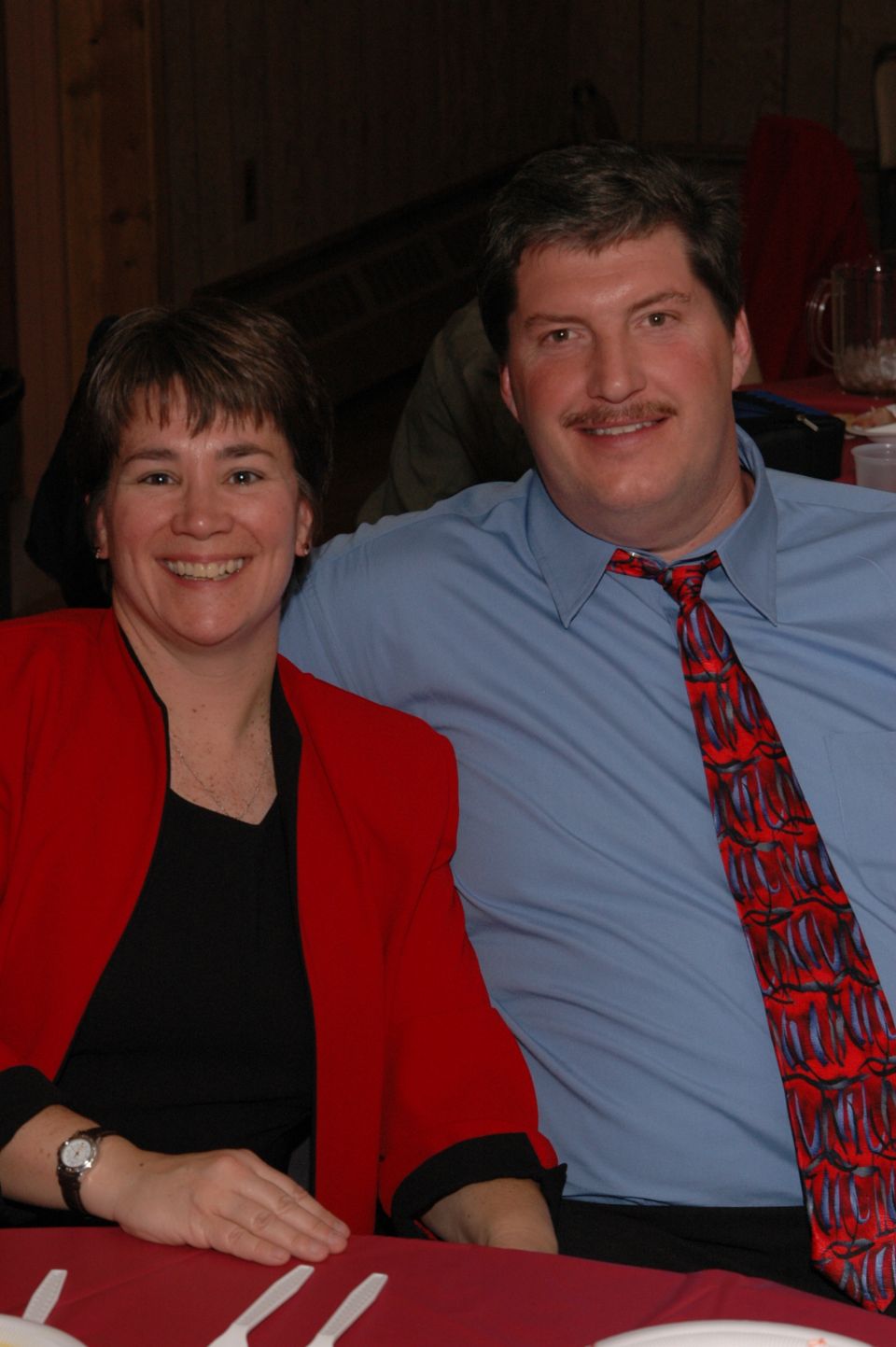 Woman in red jacket and man in blue shirt with patterned tie sit at a table
