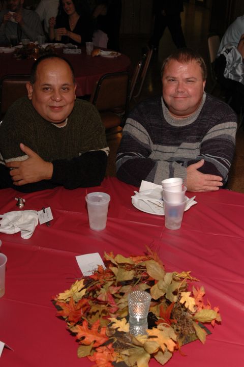 1985 Ford Crown Victoria LTD - Two men are seated at a table covered with a red tablecloth, with a decorative arrangement of autumn leaves in the foreground.