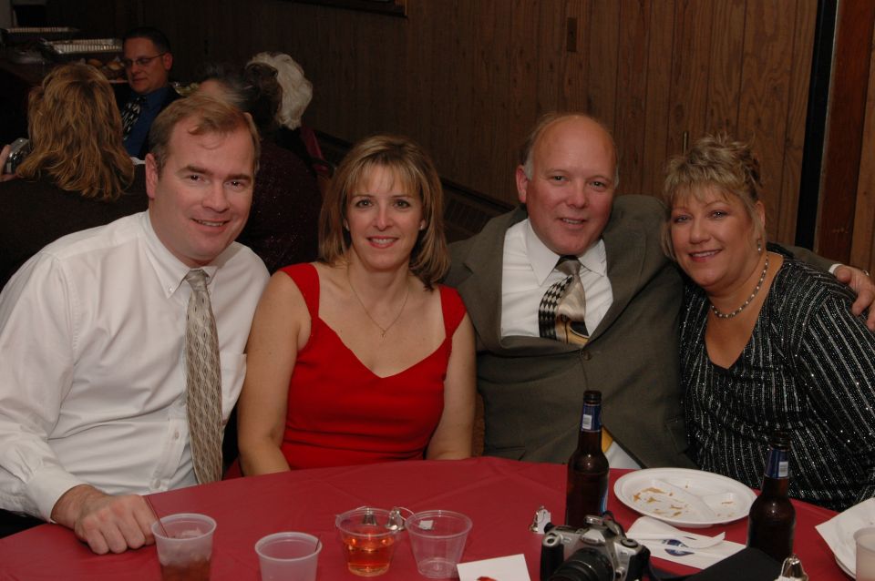 Four adults seated at a red-clothed table, with drinks and a camera visible