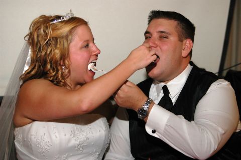 1985 Ford Crown Victoria LTD - A newlywed couple shares a playful moment feeding each other cake during their wedding reception.