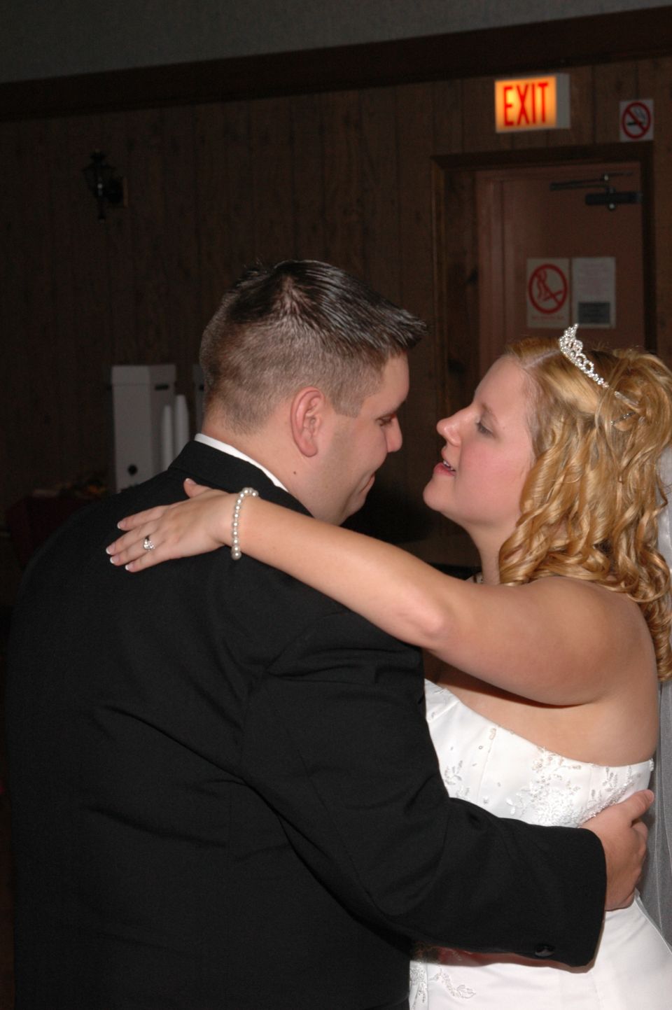 Groom in black suit dances with bride in white wedding dress, both wearing rings