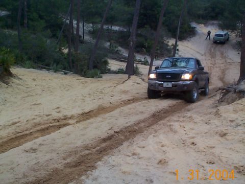 1992 Ford Bronco - Two vehicles navigate a sandy trail in a wooded area.