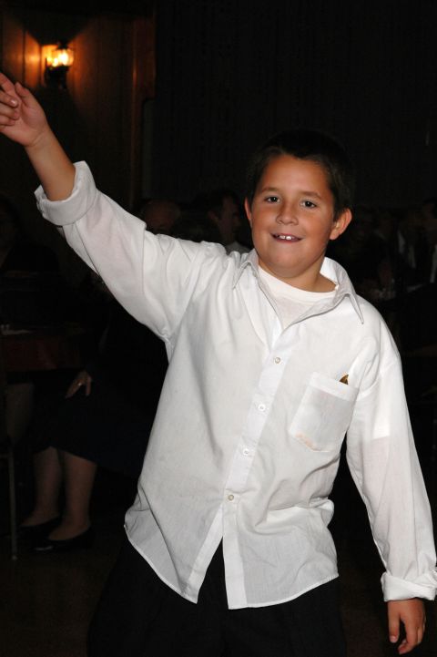 1985 Ford Crown Victoria LTD - A young boy in a white dress shirt with his arm raised in celebration at an event.