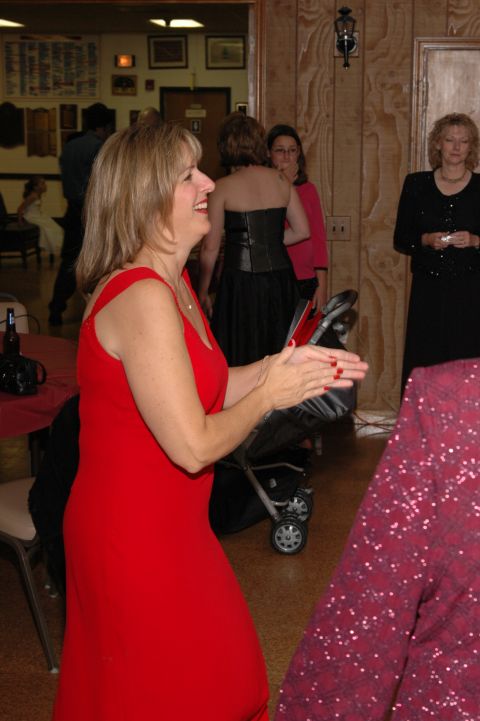1985 Ford Crown Victoria LTD - A woman in a red dress claps her hands while attending an indoor event with other guests.