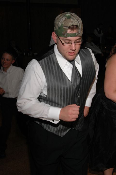 1985 Ford Crown Victoria LTD - A man wearing a tuxedo vest and a camouflage baseball cap dances at a wedding reception.