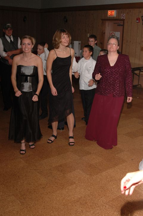 1985 Ford Crown Victoria LTD - A group of people, including women in dresses and children, are dancing in a room with wood-paneled walls.