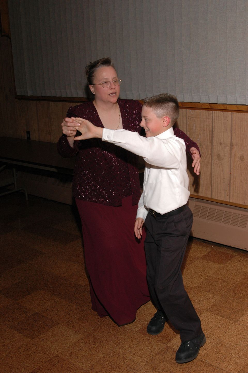 Woman in a maroon dress and a boy in a white shirt and black pants dance together