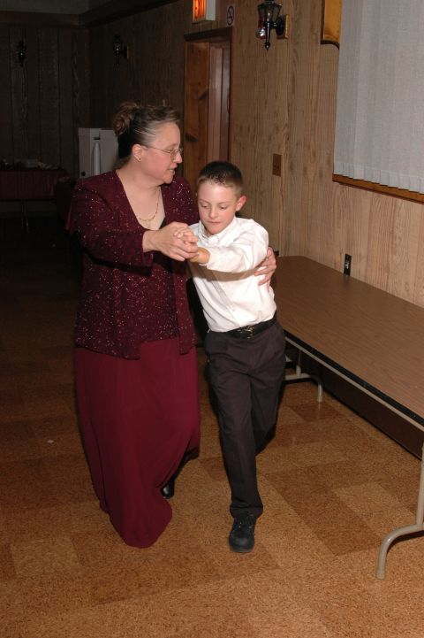 1985 Ford Crown Victoria LTD - A woman and a young boy are captured mid-dance in a room with wooden walls and a table along the side.