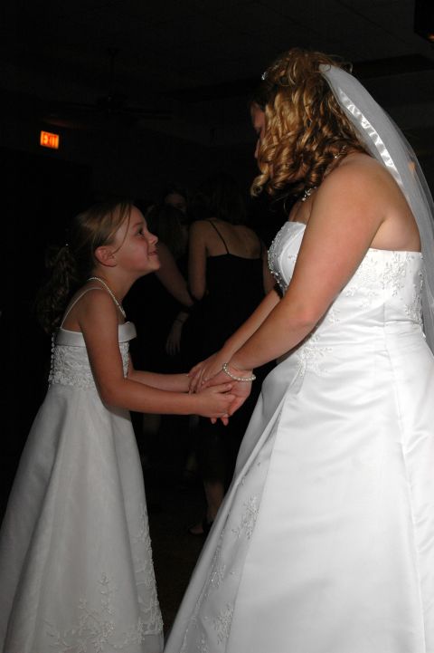 Bride and flower girl in white dresses holding hands at a wedding reception