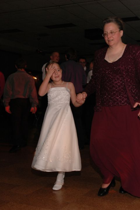 young girl in a white dress and an adult woman in a burgundy dress hold hands while dancing