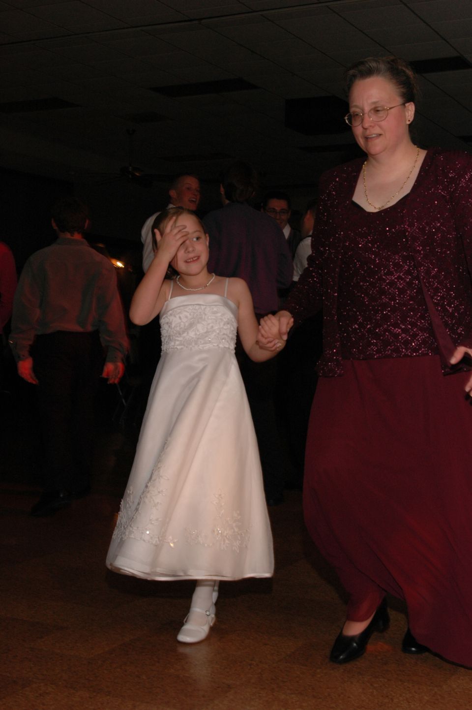 young girl in a white dress and an adult woman in a burgundy dress hold hands while dancing