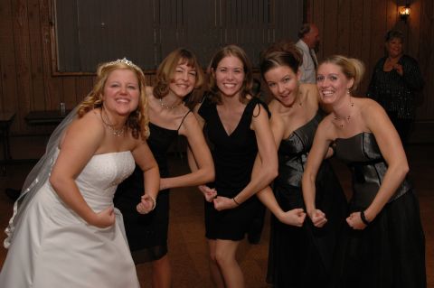 Bride in white dress and four bridesmaids in black dresses flex their biceps