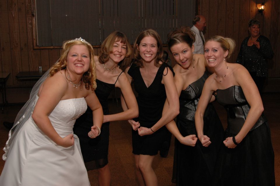 Bride in white dress and four bridesmaids in black dresses flex their biceps